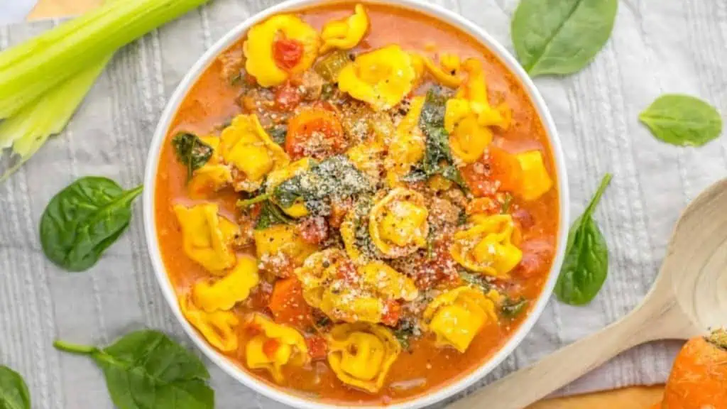a white bowl filled with a cream sausage based broth and cooked tortellini