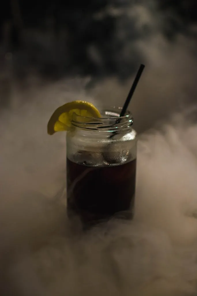 A mysterious, smoky cocktail garnished with a lemon slice and straw, creating a refreshing and mystical atmosphere.
