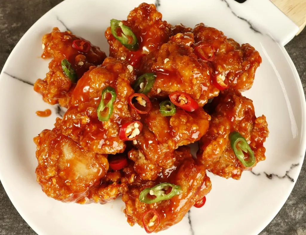 Delicious spicy fried chicken garnished with green peppers on a marble plate.