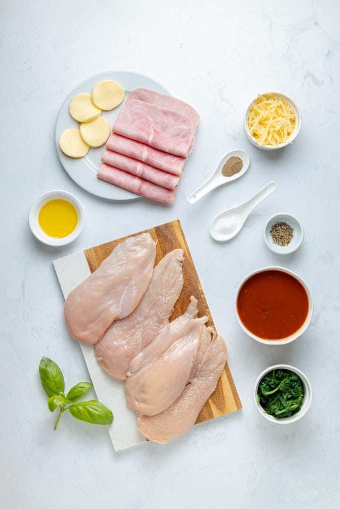 Close-up of a chicken roll up ingredients that show fresh basil, marinara, ham, cheeses, and spinach