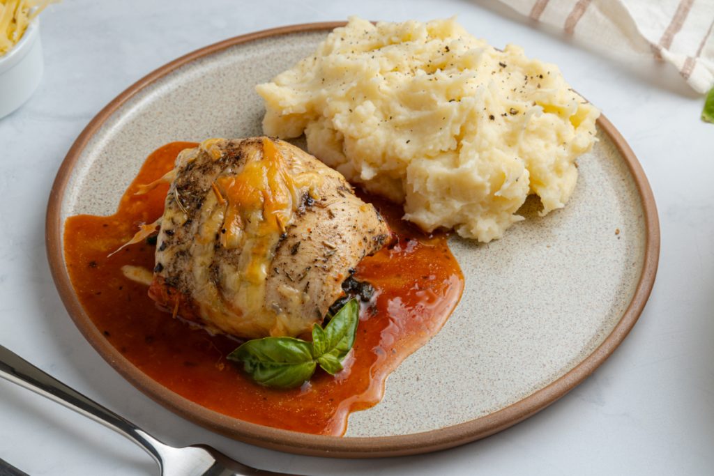 Close-up of a chicken roll up topped with fresh basil and sauce
