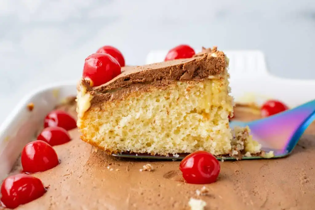 Spatula lifting a slice of poke cake from the pan with cherries
