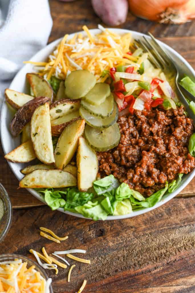 Sloppy joe bowl with lettuce, roasted potato wedges, peppers and onions, cheese, and pickles