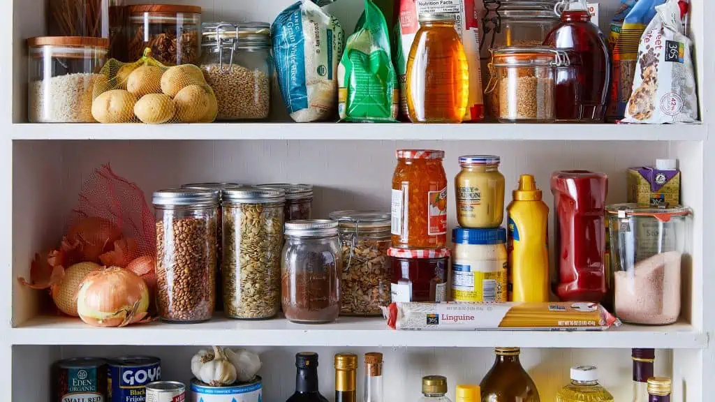 shelves full of pantry staples of onions, potatoes, mustard, hams, mayo, seeds, beans, rice, honey, chocolate chips, and canned vegetables.
