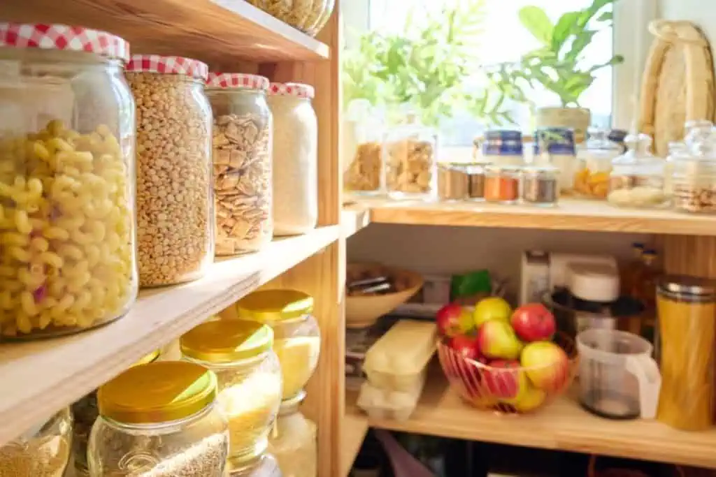 wooden shelves filled with jars of pantry staple items from dried pasta, dried beans, rice, and otehr cooking ingredients