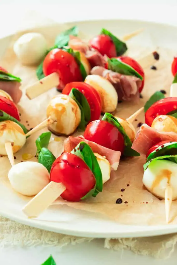 Caprese skewers with prosciutto, mozzarella balls, and cherry tomatoes drizzled with balsamic glaze.