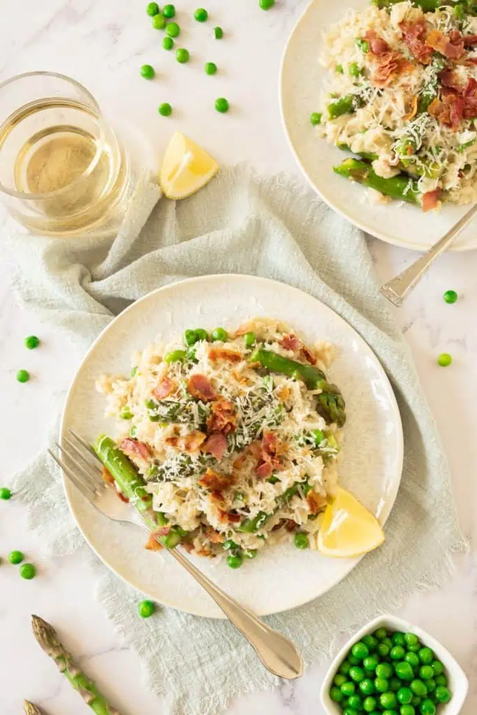 Over head view of creamy asparagus risotto on a cream colored plate with crumbled bacon and topped with grated parmesan and slice of lemon