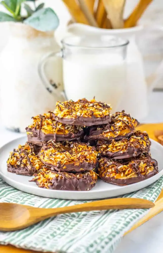 Stack of homemade Samoas cookies on a white plate showing the toasted coconut layer, dark chocolate-dipped base, and thin chocolate drizzle over the top.