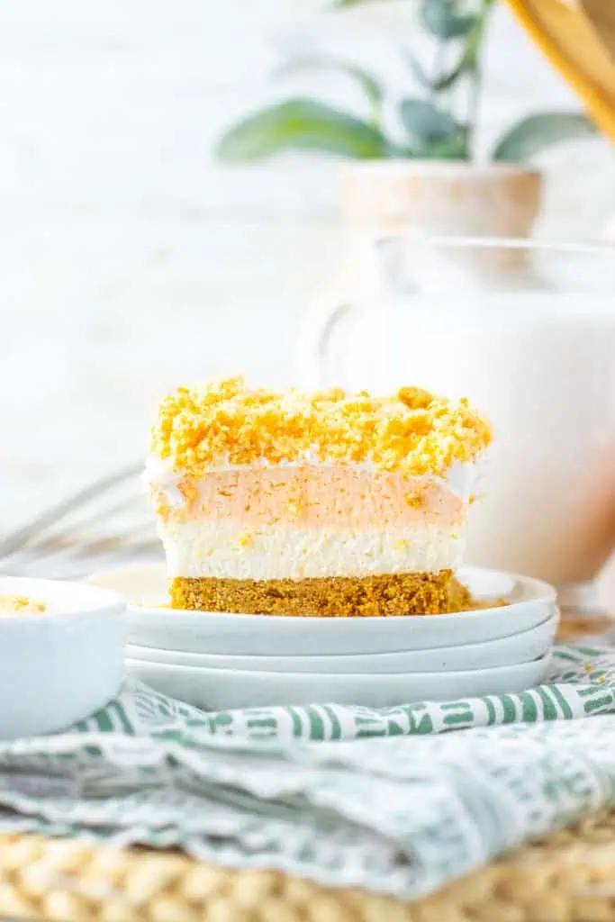 Orange creamsicle crunch bars sliced and stacked on a white plate showing the golden graham cracker crust, creamy white and orange layers, and vibrant orange vanilla Oreo crunch topping.