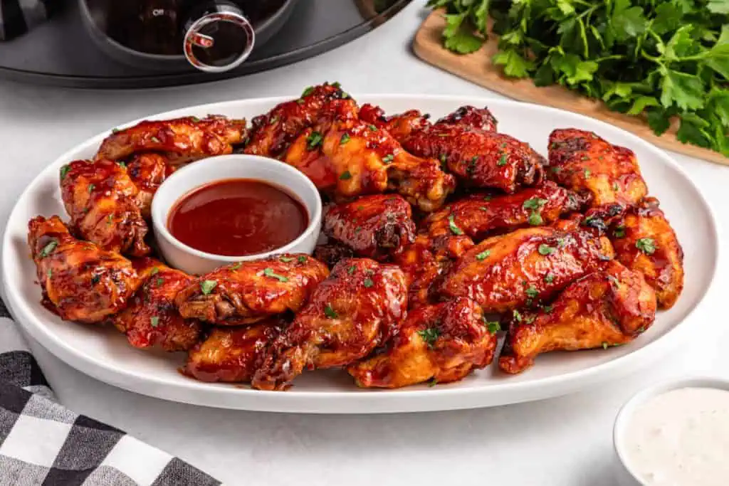 Sticky slow cooker BBQ chicken wings glazed with caramelized sauce and garnished with parsley on a serving platter.
