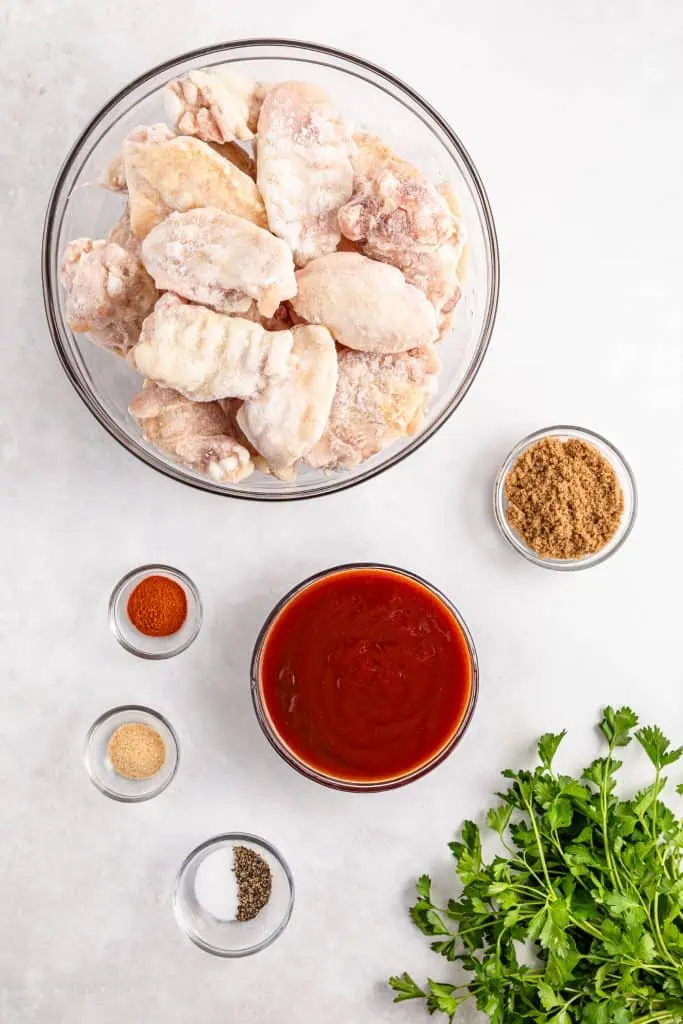 Ingredients for slow cooker BBQ chicken wings arranged overhead with chicken wings, BBQ sauce, brown sugar, and seasonings.
