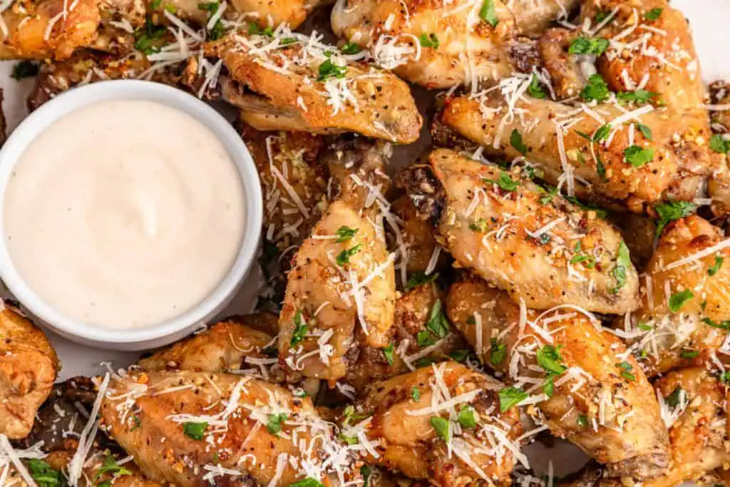 Chicken wings, butter slices, grated parmesan, minced garlic, parsley, and seasonings arranged overhead with a dipping sauce