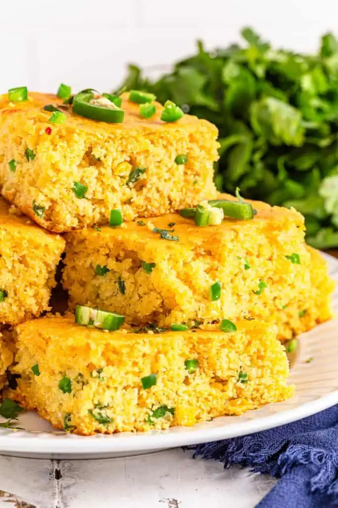 Close-up cross-section of cheddar jalapeno cornbread stacked on top of each other, showing a moist, cheesy crumb with visible jalapeno pieces and melted pepper jack cheese throughout
