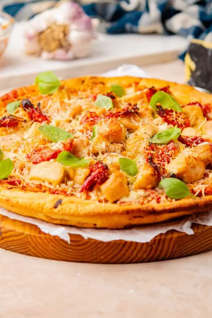 Marry me chicken pizza whole on a wooden cutting board, cheese golden and bubbling, sun-dried tomatoes and chicken visible, fresh basil scattered over after baking