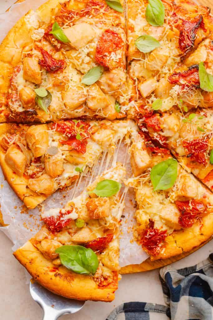 Close-up of marry me chicken pizza cheese pull, golden mozzarella stretching between two slices being pulled apart