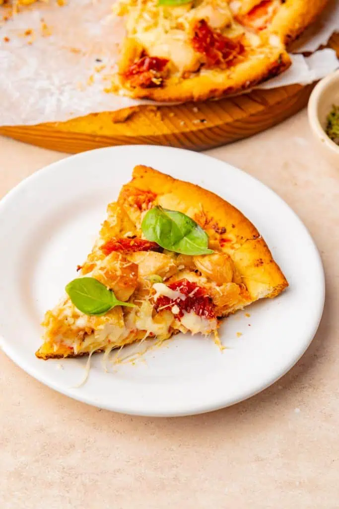 slices of marry me chicken pizza on a white plate, fresh basil garnish, glass of white wine alongside, evening lighting