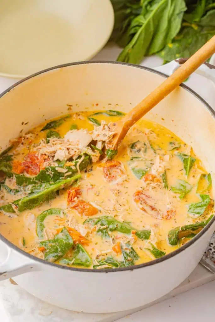 Baby spinach leaves being dropped into the golden marry me soup base in the final 60 seconds, steam rising from the surface