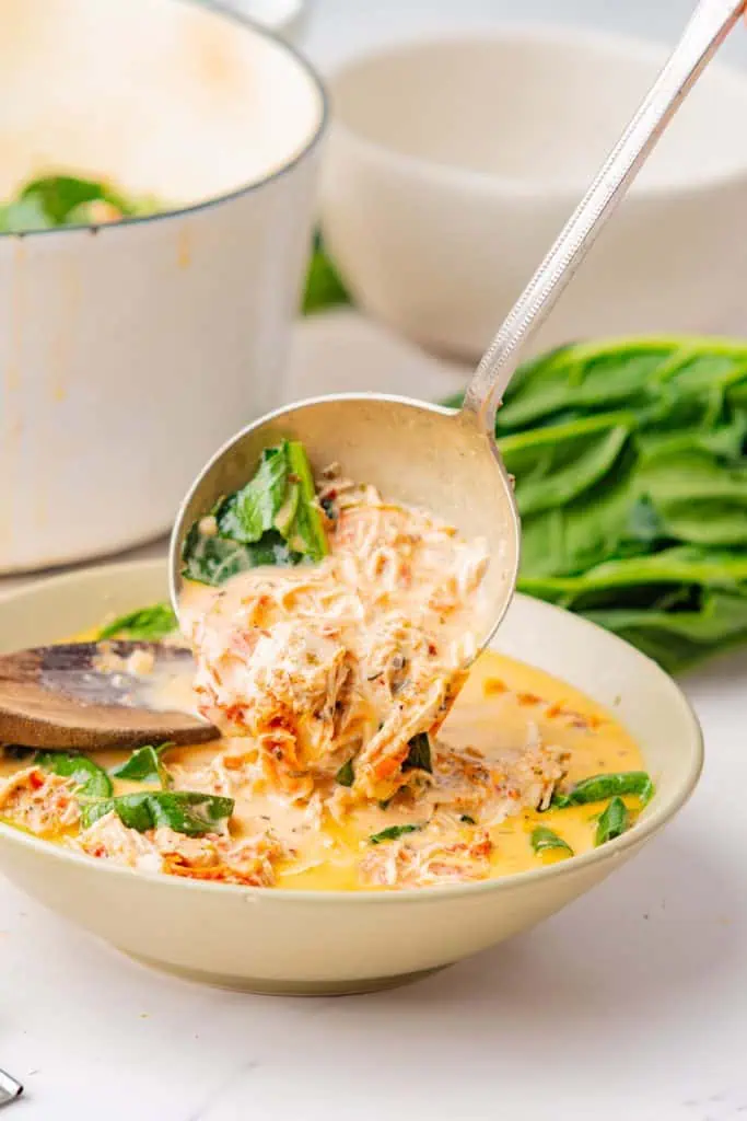 Wide shallow bowl of marry me chicken soup with vivid green spinach, golden cream broth, and shaved Parmesan visible on top, photographed from above