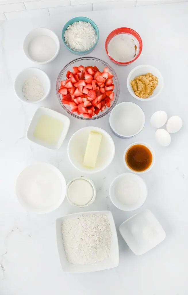Fresh strawberries, all-purpose flour, unsalted butter, eggs, sour cream, buttermilk, and sugar arranged on a white marble surface for strawberry crumb cake