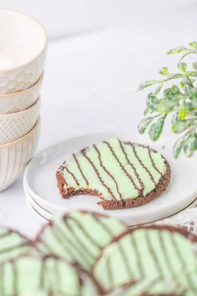 Thin mint chocolate cookies stacked on a white plate with green peppermint frosting and glossy chocolate drizzle on top