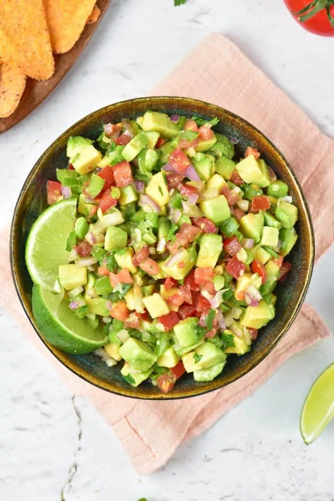 Large bowl of chunky avocado salsa with visible diced avocado cubes, tomato, and cilantro, served with tortilla chips on a wooden board