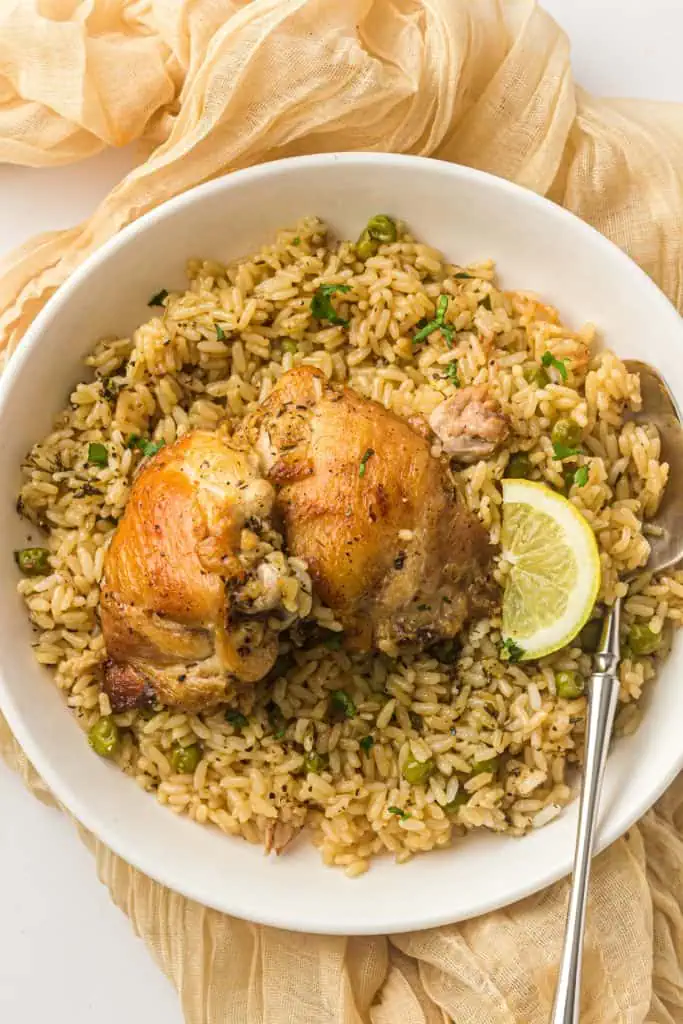 Two bone-in chicken thighs served over Instant Pot rice in a white bowl with a lemon wedge and fork, shot from a slight angle on a white surface