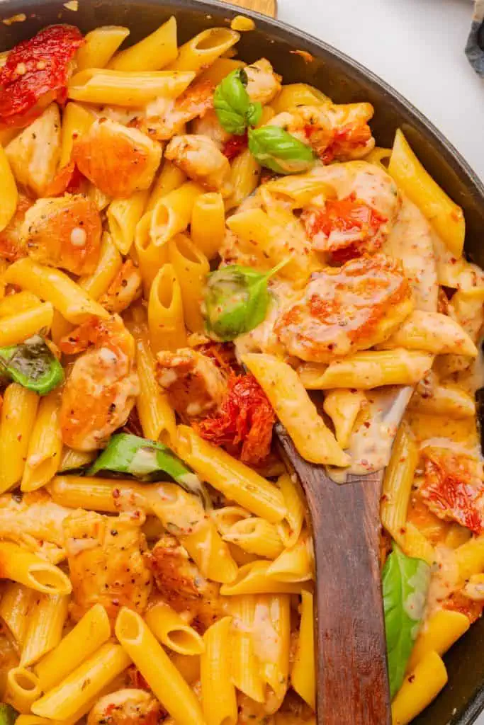 pan of marry me pasta on a linen-covered table with fresh pieces of basil to garnish on a dark wooden spoon