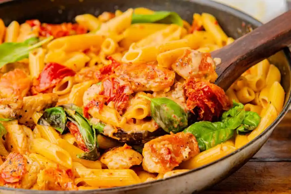 tossing rigatoni with cream sauce in a stainless steel skillet, sauce clinging to pasta ridges as it emulsifies
