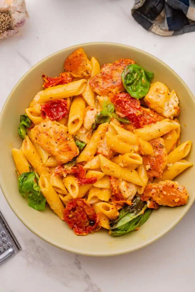 Marry me pasta piled high in a sage ceramic bowl, glistening with creamy sun-dried tomato sauce, topped with fresh Parmesan shavings and basil