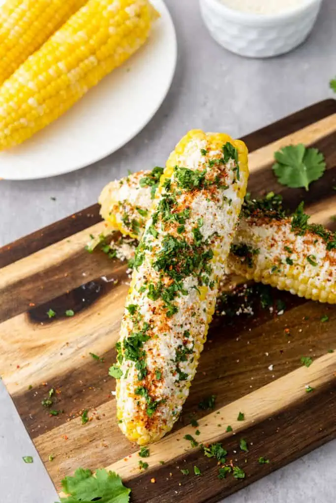 Extreme close-up of elote corn showing the creamy crema and mayo coating, crumbled cotija cheese, and tajin dusted across the surface