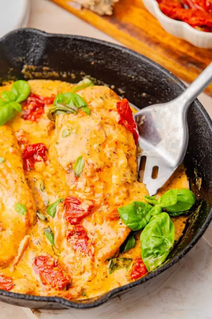 Close-up of thick creamy marry me chicken sauce coating the seared breast, flecked with red sun-dried tomatoes and fresh green basil