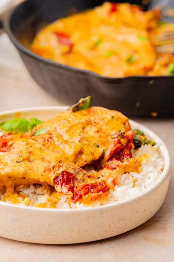 Marry me chicken served in a wide shallow bowl over white rice and a black cast iron skillet in the backround