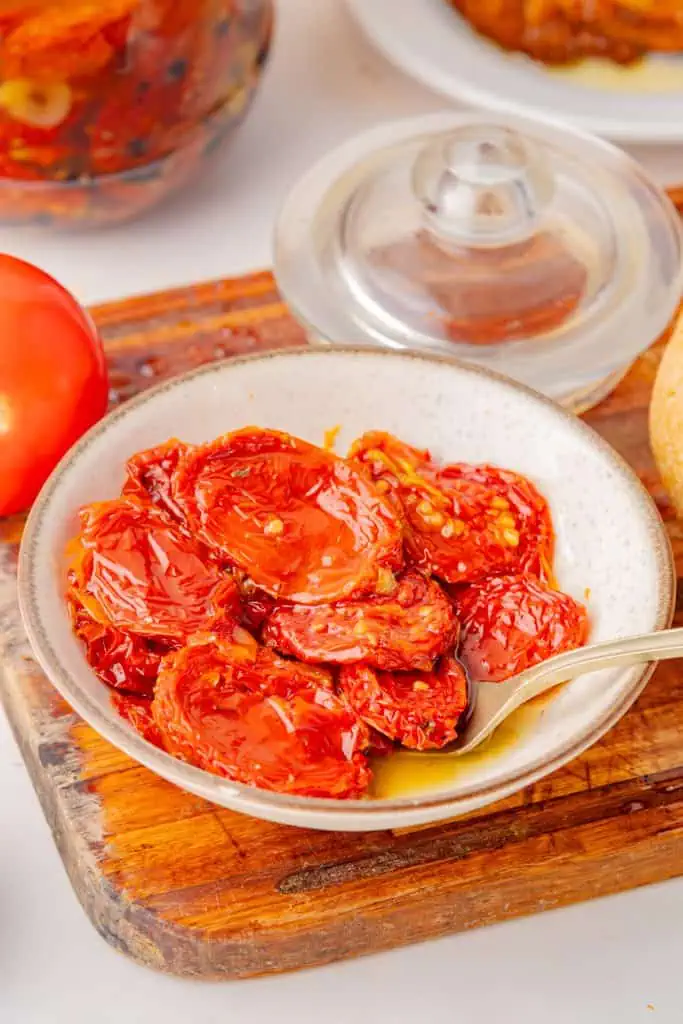 Close-up of oil-packed sun-dried tomatoes glistening with golden olive oil and scattered black peppercorns in a glass jar