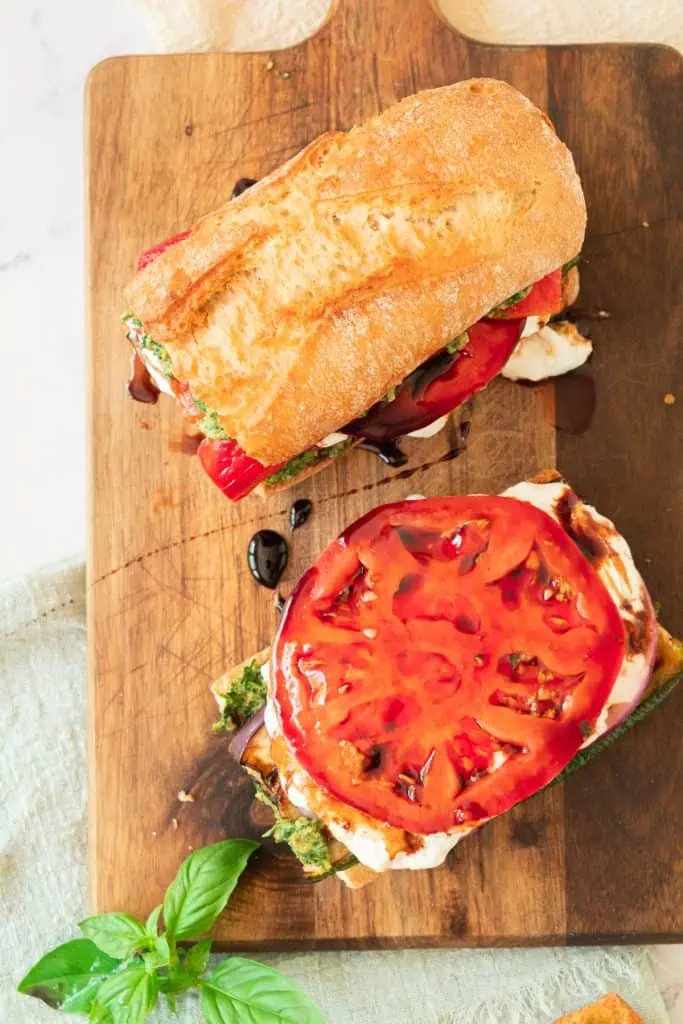 Grilled vegetable sandwich on a crusty baguette stacked with charred zucchini, eggplant, roasted red peppers, creamy burrata, and walnut pesto with balsamic glaze showing a lsiced tomato
