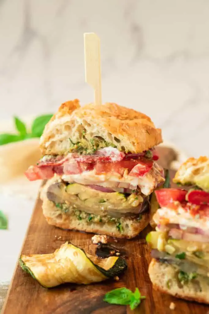 Close-up of grilled vegetable sandwich layers showing torn burrata dripping balsamic glaze over charred eggplant, zucchini, and green walnut pesto