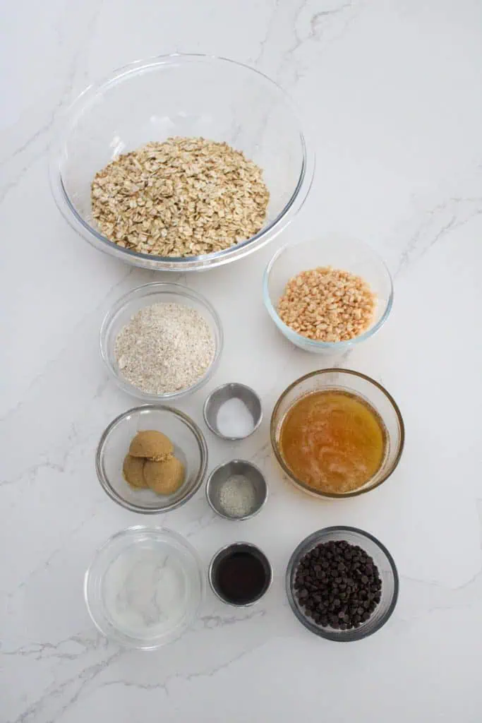 ingredients needed to make honey oat granola bars. Glass dishes with brown sugar, oats, oat flour, crispy rice cereal, honey, vanilla extract and chocolate chips