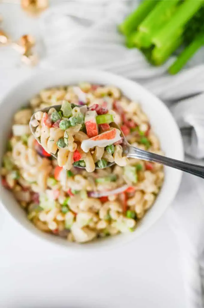 Crab pasta salad served in a white bowl on a bright kitchen counter with fresh celery and wooden serving spoons in the background