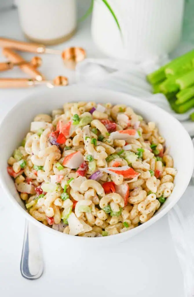 Close-up spoonful of creamy crab pasta salad showing tender elbow pasta, sweet peas, diced red pepper, and a chunk of imitation crab in Old Bay dressing