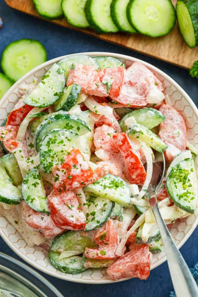 Close-up of crunchy cucumber slices and ripe tomato chunks coated in glossy sour cream dressing with cracked black pepper