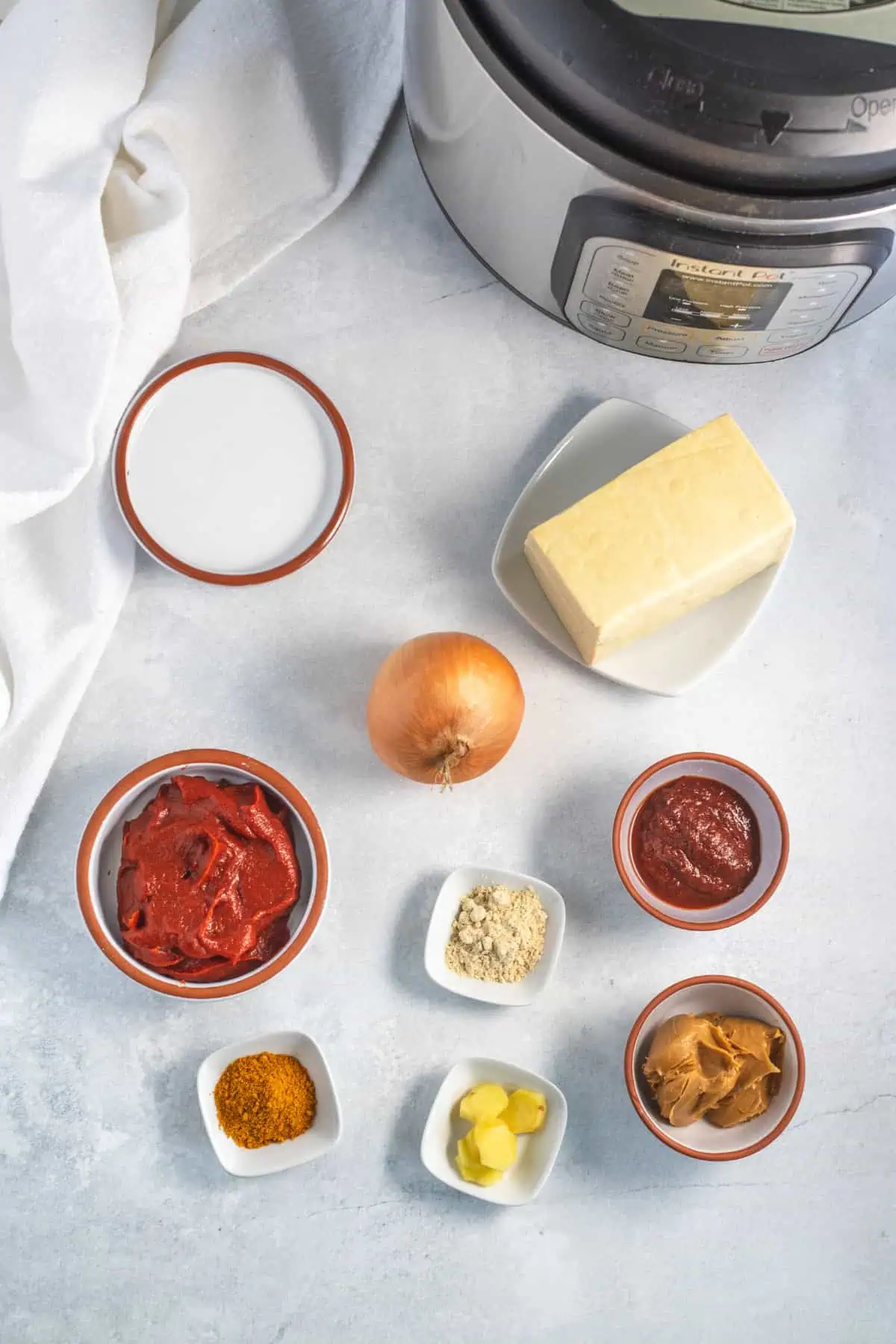 Overhead flatlay of Instant Pot tofu curry ingredients with cubed tofu, coconut milk, tomato paste, red curry paste, onion, and ginger