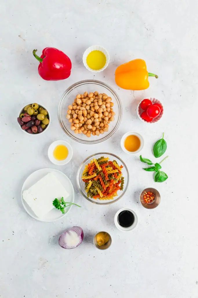 Mediterranean pasta salad ingredients arranged overhead with rotini pasta, kalamata olives, bell peppers, cherry tomatoes, chickpeas, feta, and red onion