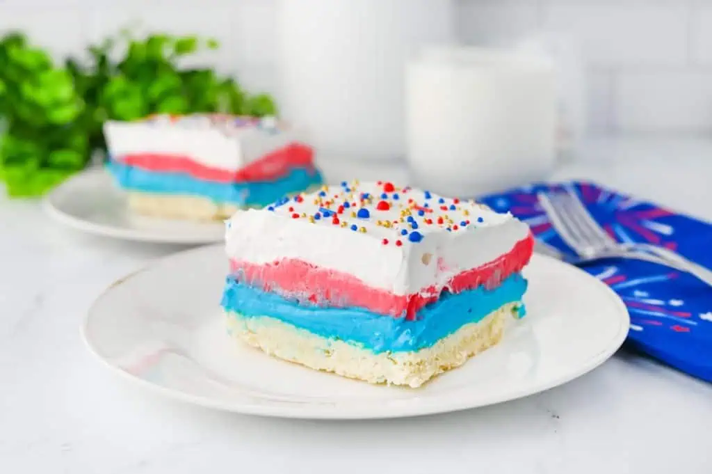 Close-up of 2 slices of red white and blue lush layers with crisp stripes of blue cheesecake, red pudding, and fluffy white whipped topping on shortbread crust