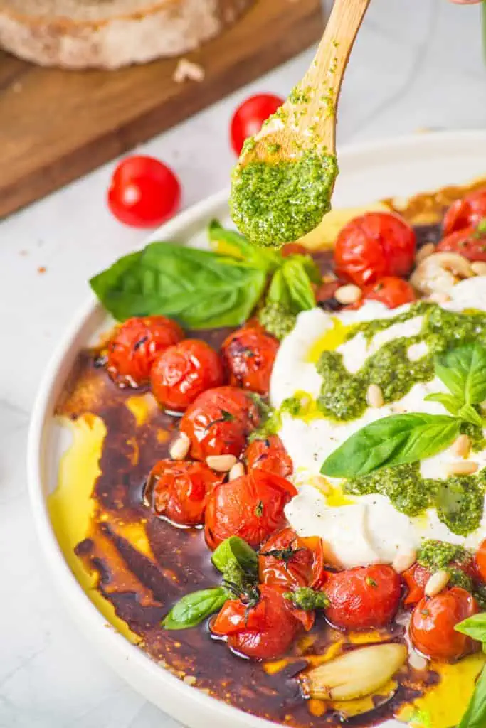 Close-up of opened burrata spilling over blistered cherry tomatoes with pesto drizzle, pine nuts, and glossy honey balsamic pan juices