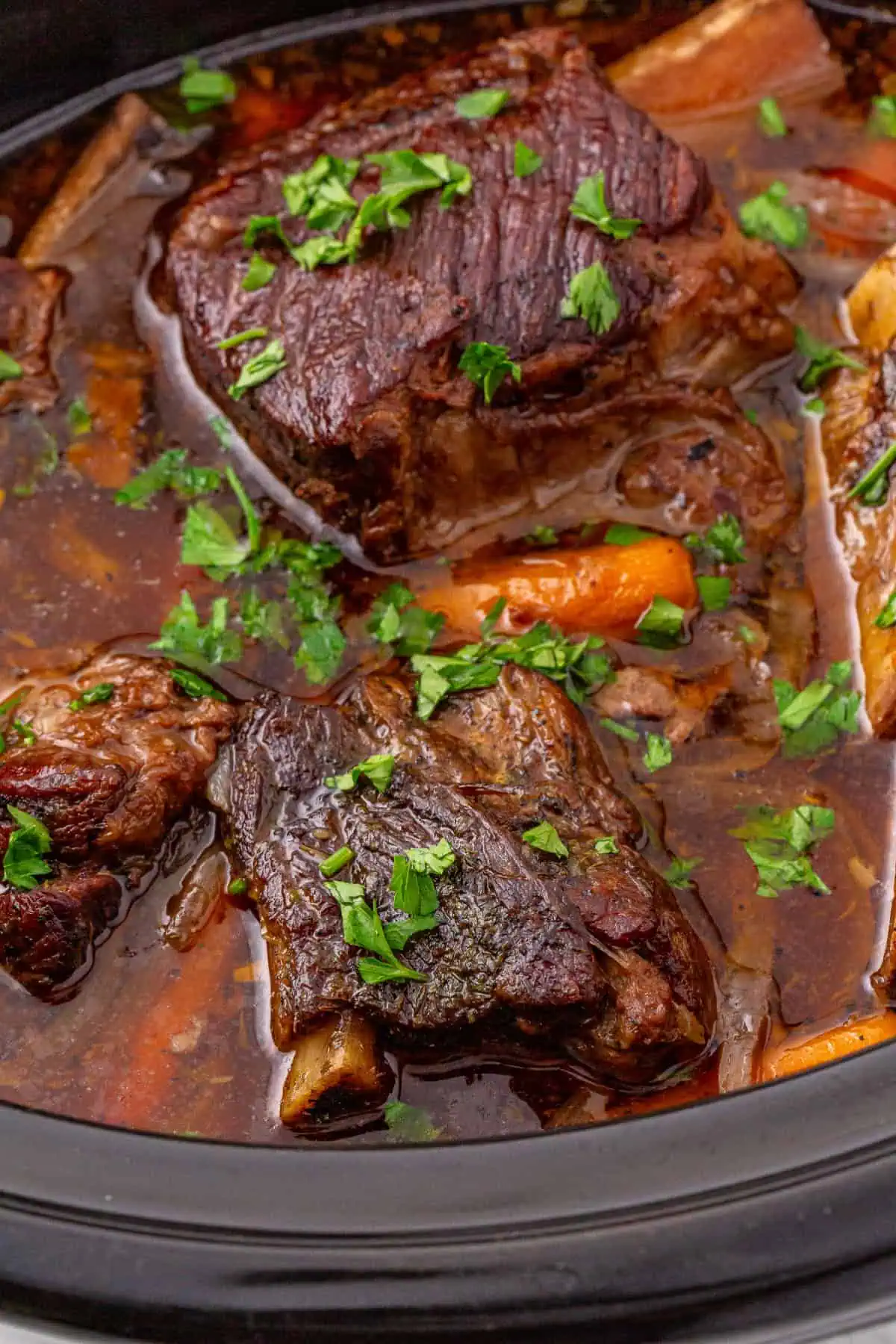 Tender slow cooker beef short ribs with carrots and onions in a black crockpot liner