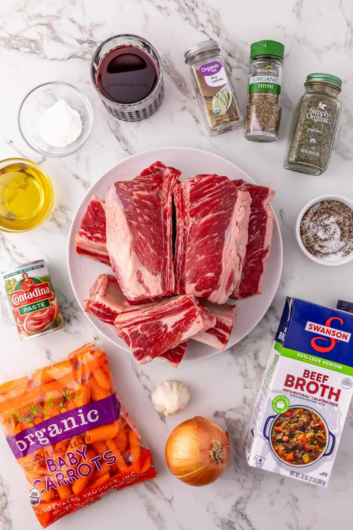 Bone-in beef short ribs, baby carrots, red wine, tomato paste, and herbs laid out for crockpot beef short ribs