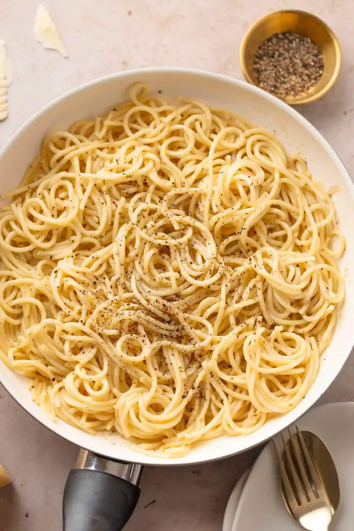 Close-up of silky cacio e pepe sauce coating strands of spaghetti in a pan