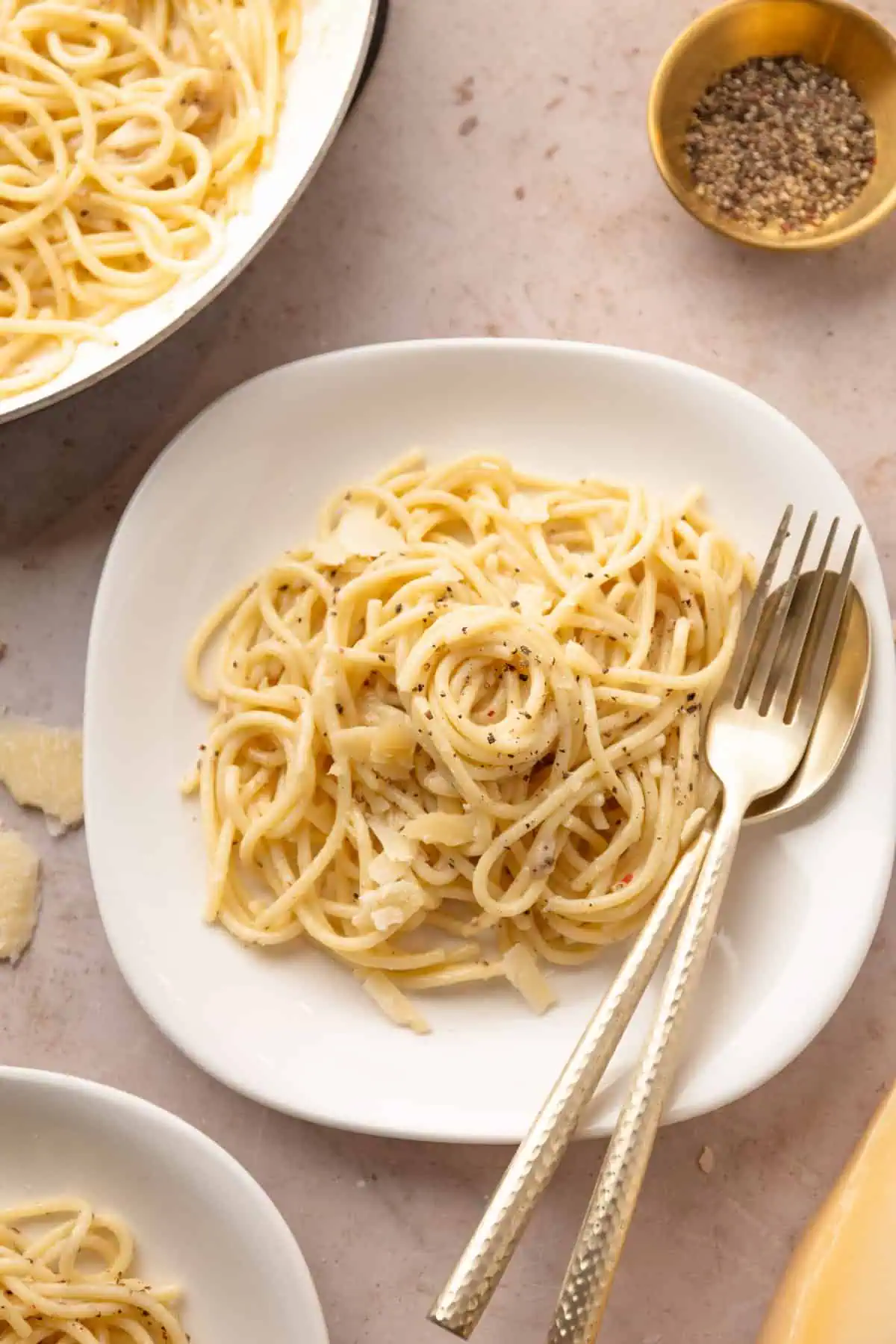 A bowl of creamy cacio e pepe twirled with a fork and spoon and topped with cracked black pepper