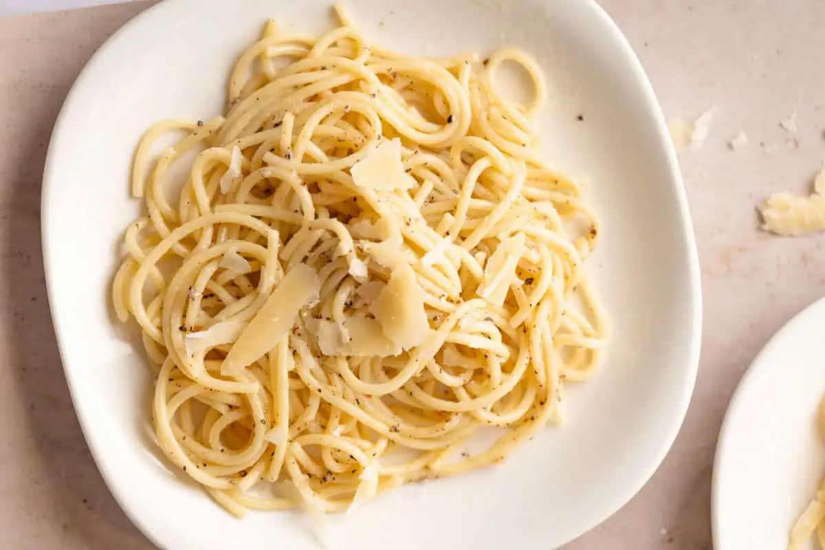 Cacio e pepe plated in a shallow bowl with extra grated parmesan and pepper