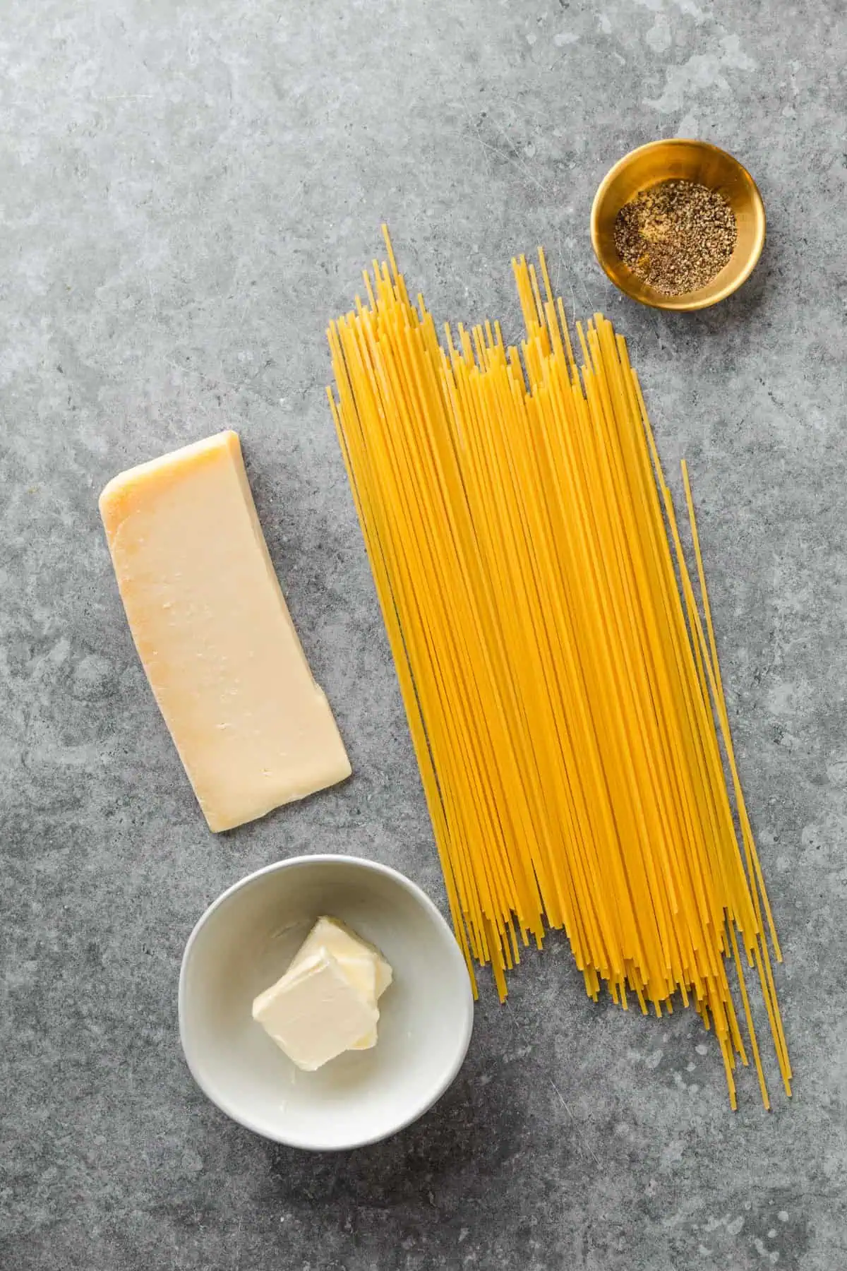 Spaghetti, a wedge of parmesan, butter, and black peppercorns laid out for cacio e pepe