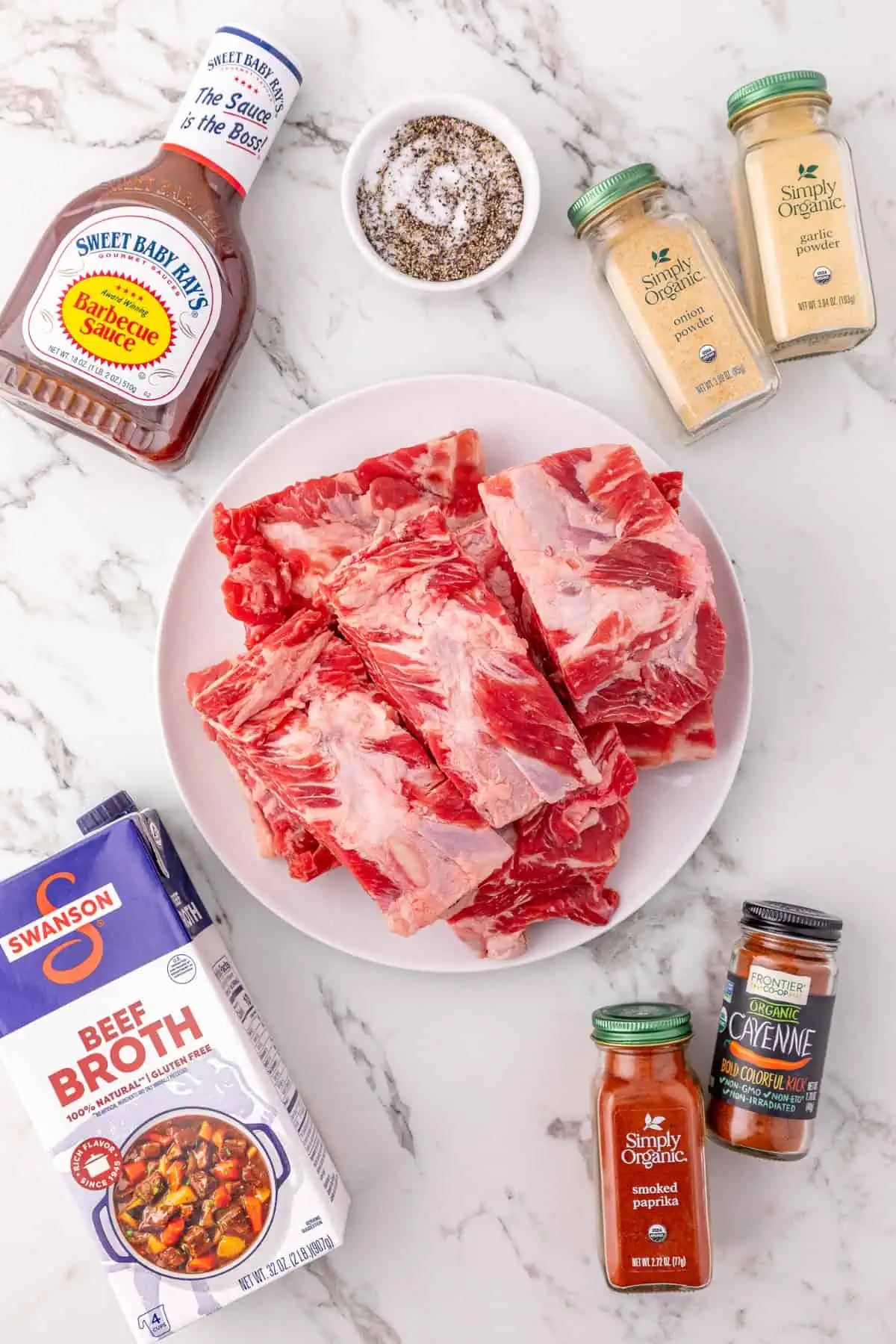 Beef back ribs, smoked paprika, garlic powder, and a bottle of BBQ sauce laid out for crockpot BBQ beef ribs